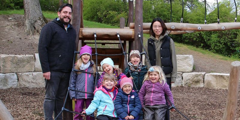 Zwei Erwachsene und fünf Kinder vor einem Klettergerüst auf einem Spielplatz 
